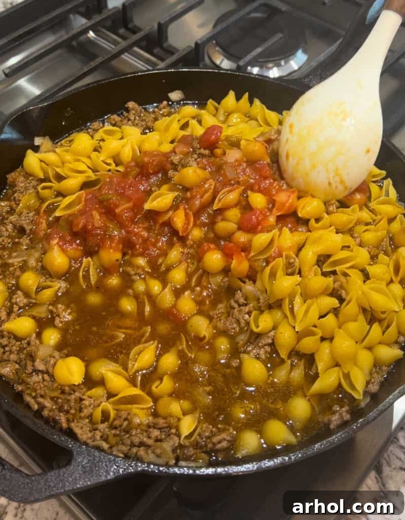 Quick One-Pot Cheesy Taco Pasta 5 Adding uncooked shell pasta, beef broth, and salsa to the browned ground beef in the skillet.
