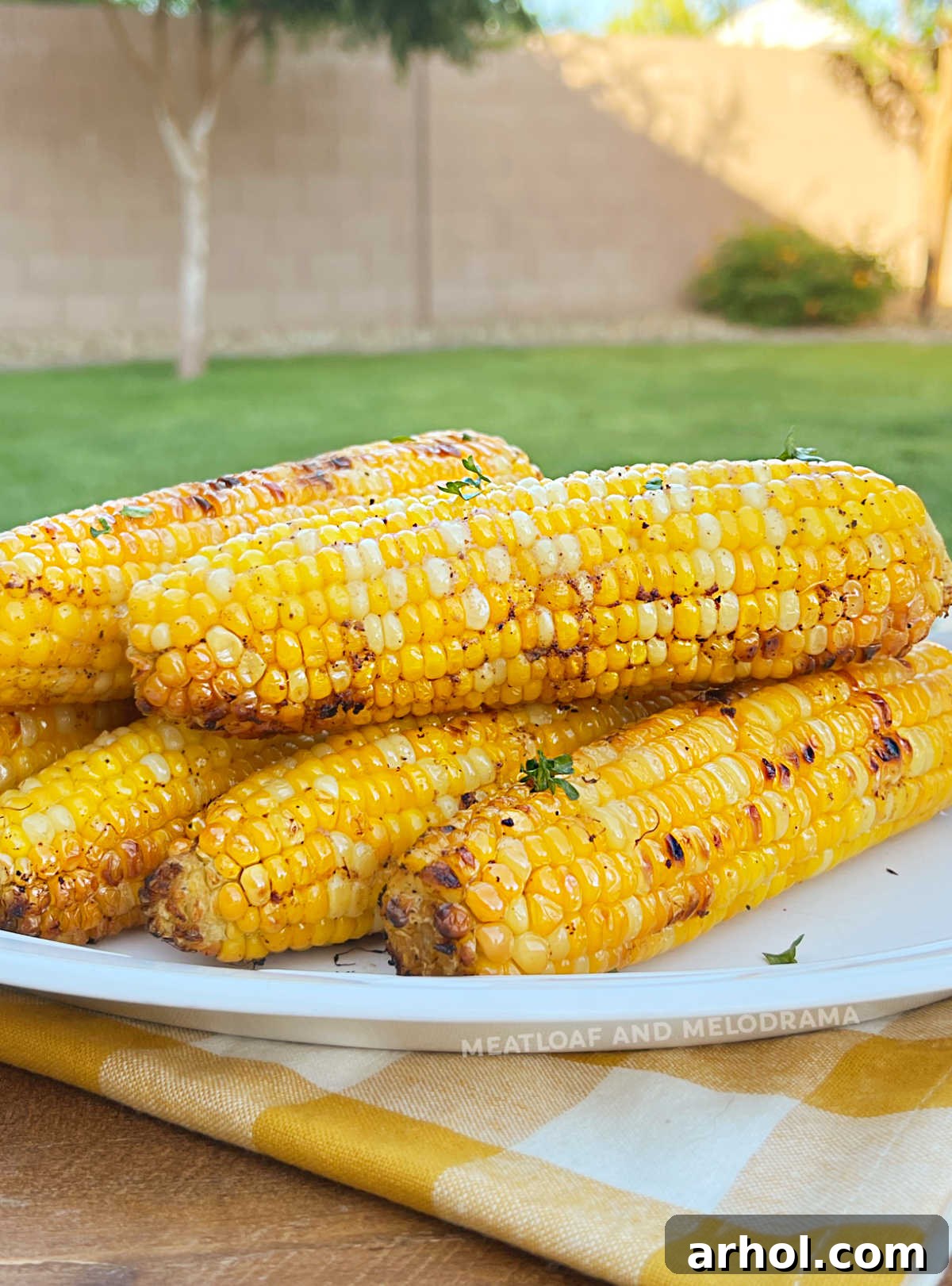 Grilled corn on the cob in foil on a platter outside by a grill