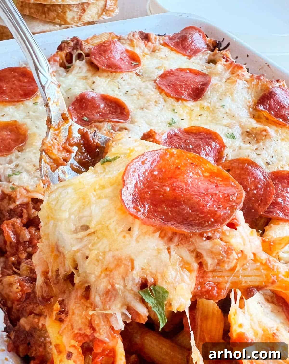 A generous scoop of pepperoni pizza pasta bake, showcasing melty cheese, crispy pepperoni, and savory sausage, ready to be served from a baking dish.