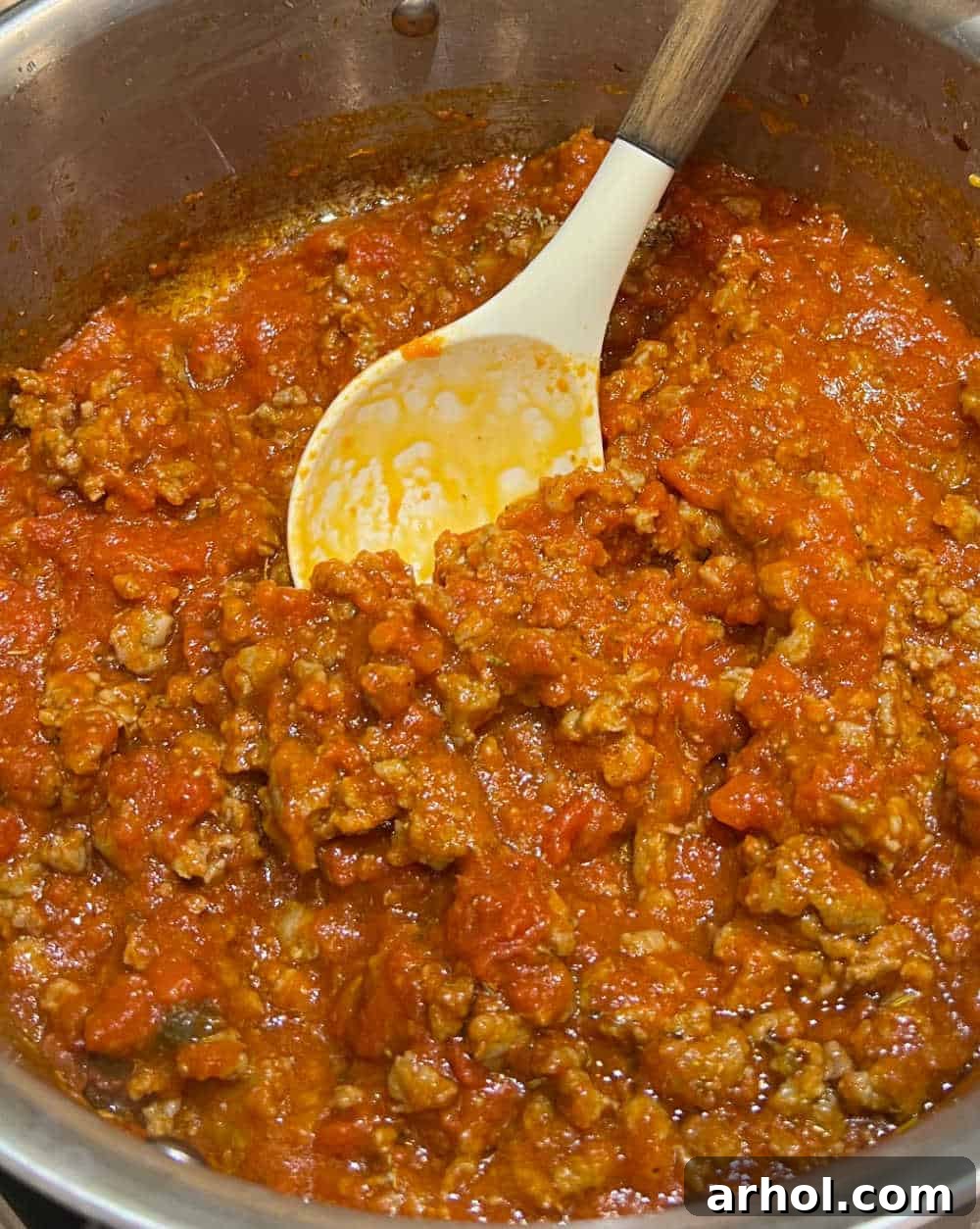 The savory mixture of cooked Italian sausage and marinara sauce simmering in a large pan.