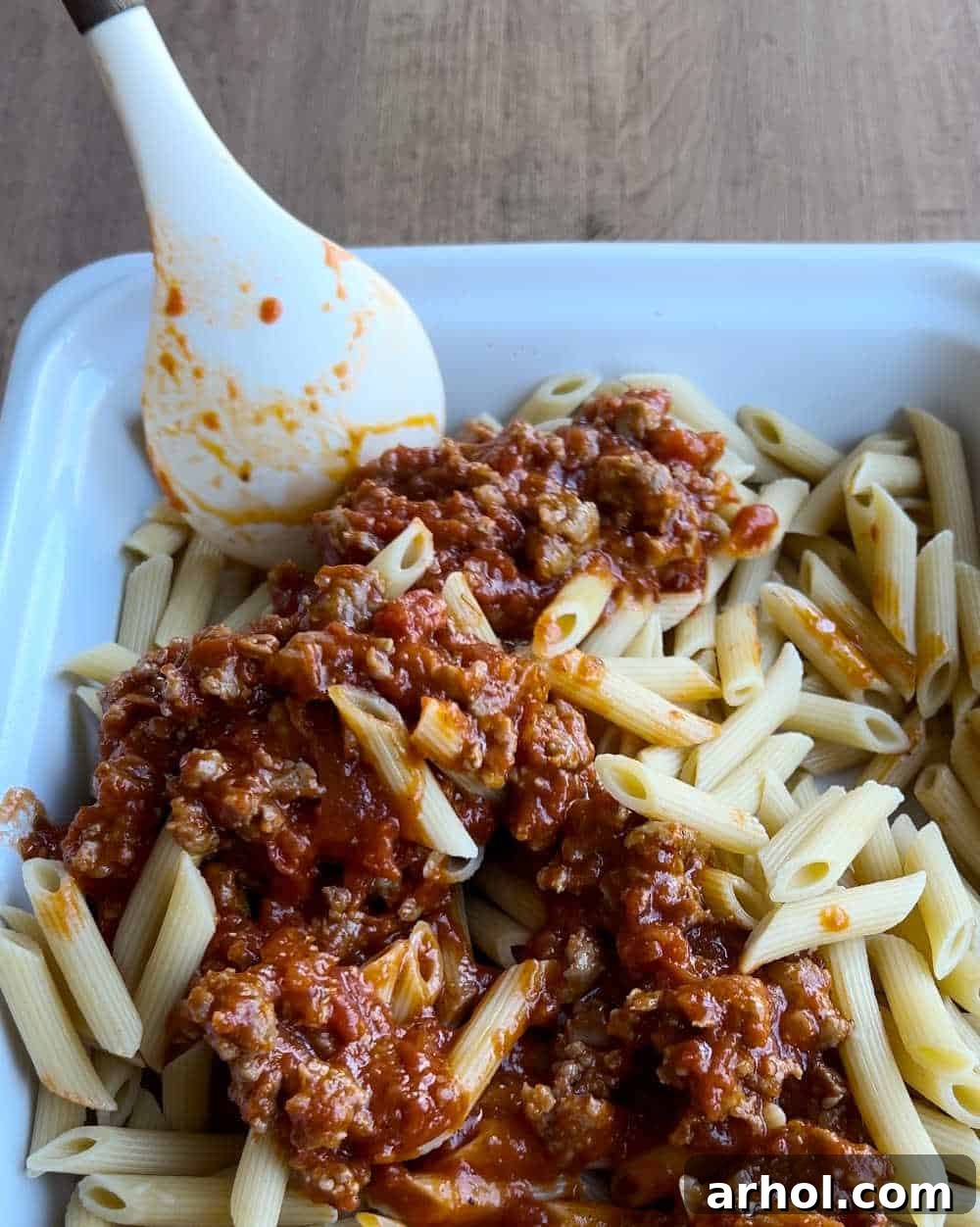 Cooked penne pasta mixed with half of the sausage and marinara sauce, spread evenly in a baking dish.