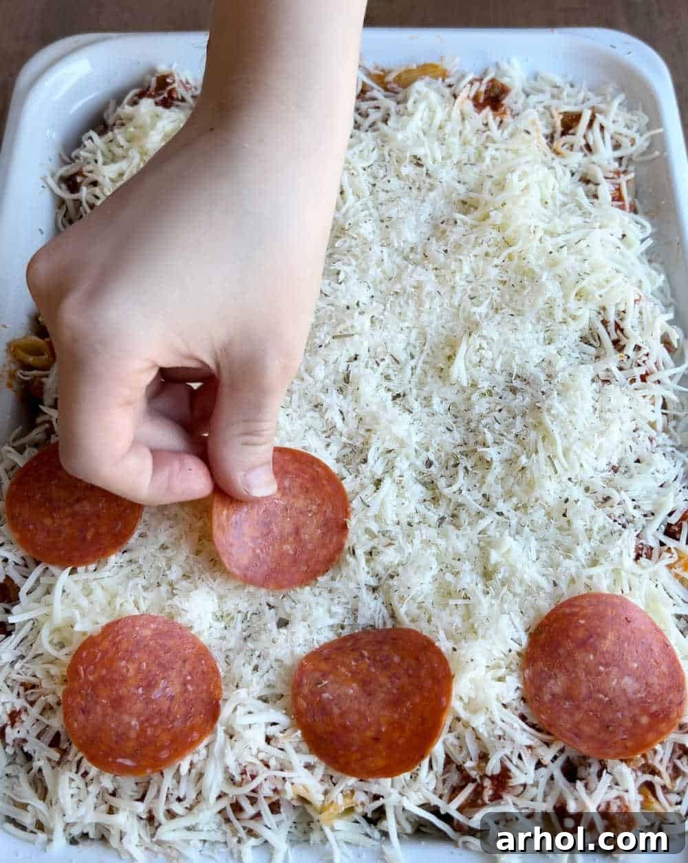 The assembled casserole topped with shredded mozzarella, grated Parmesan cheese, and pepperoni slices, ready for baking.