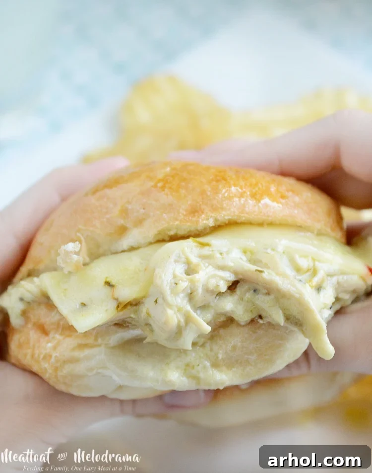 Hands holding a Crock-Pot salsa verde chicken slider, showing the cheesy filling
