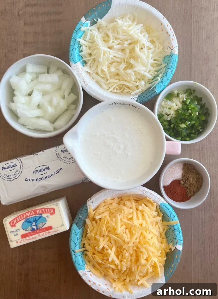 A selection of fresh ingredients laid out for homemade queso: cream cheese, butter, chopped onion, minced garlic, sliced jalapeño pepper, shredded pepper jack cheese, heavy cream, and shredded cheddar cheese.