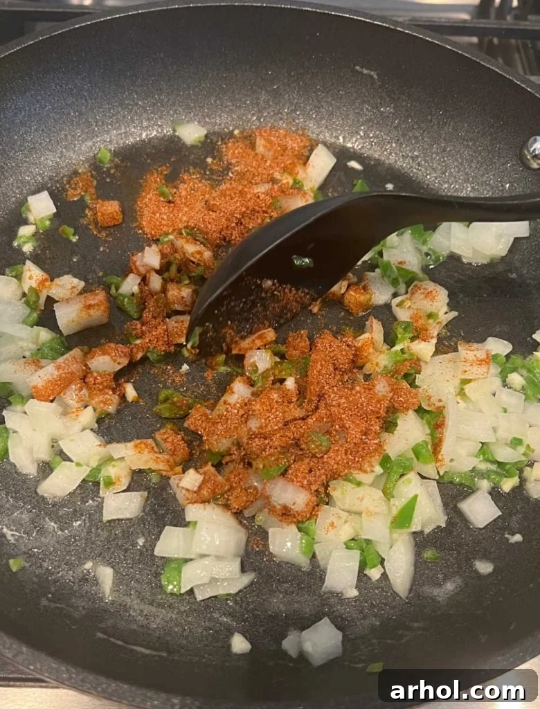 Chopped onion, jalapeno pepper, and various spices sautéing in butter in a cast iron skillet, releasing fragrant aromas.