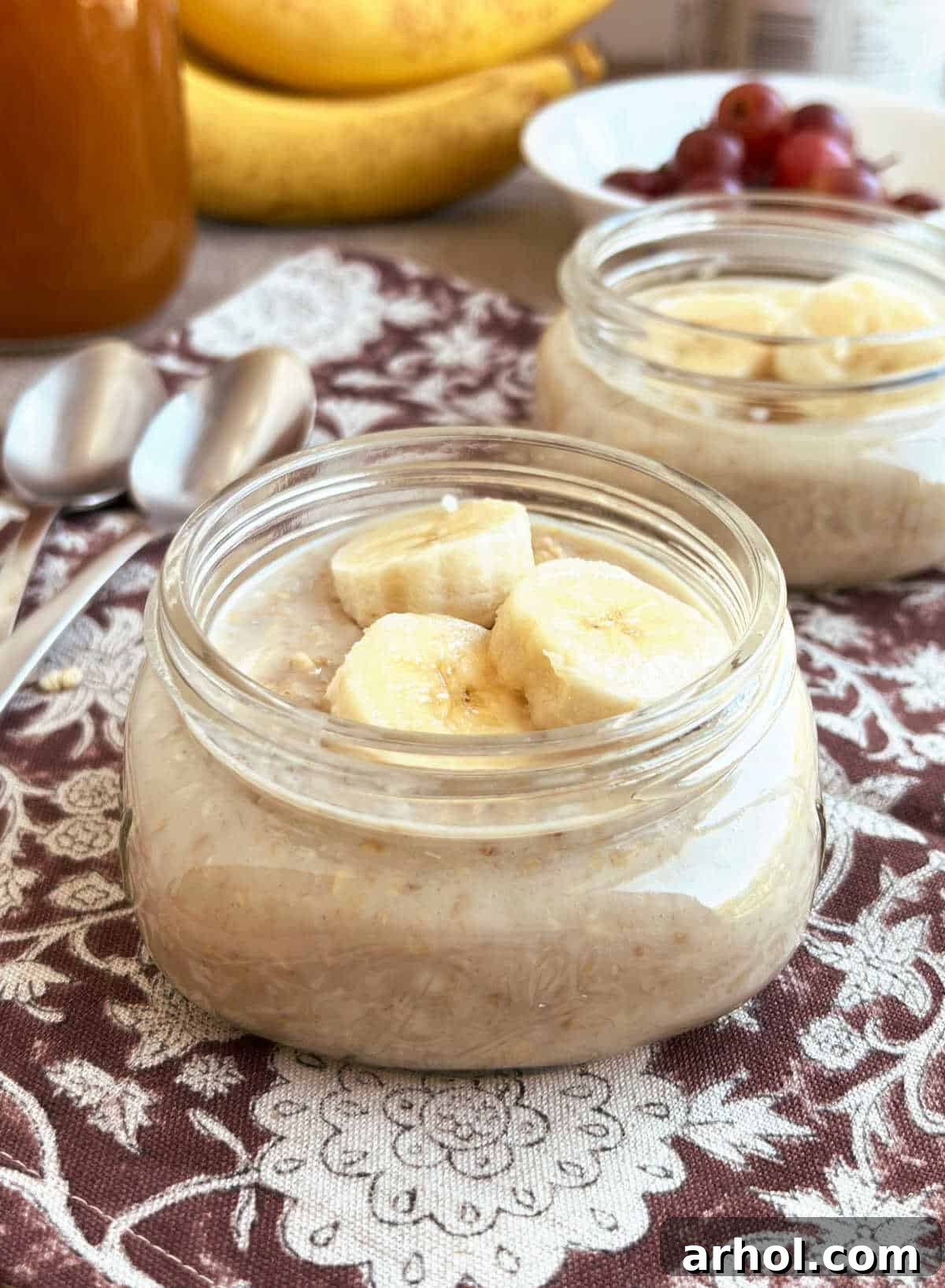 Two mason jars filled with maple brown sugar overnight oats, topped with fresh banana slices, arranged on a rustic wooden table, evoking a cozy fall morning atmosphere.