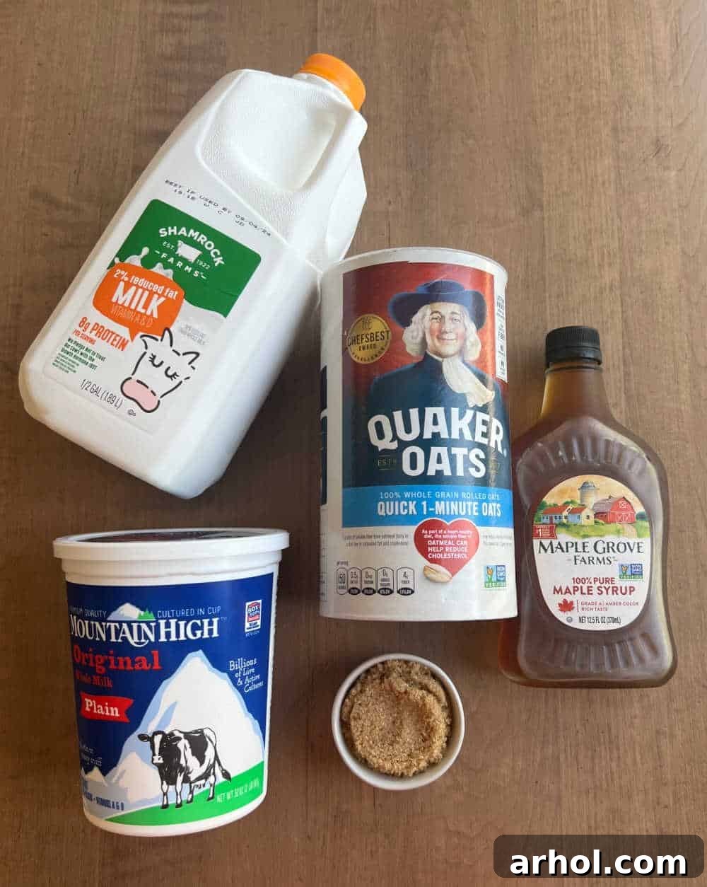 Close-up of ingredients for overnight oats: milk, quick oats, plain yogurt, brown sugar, and pure maple syrup laid out on a clean surface.