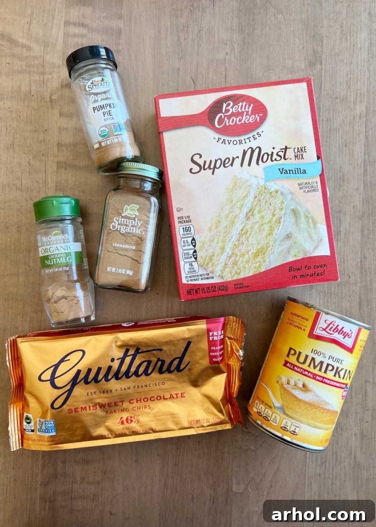 A flat lay photograph displaying the simple ingredients needed for cake mix pumpkin muffins: a box of cake mix, a can of pumpkin puree, an assortment of fall spices, and a bowl of chocolate chips.