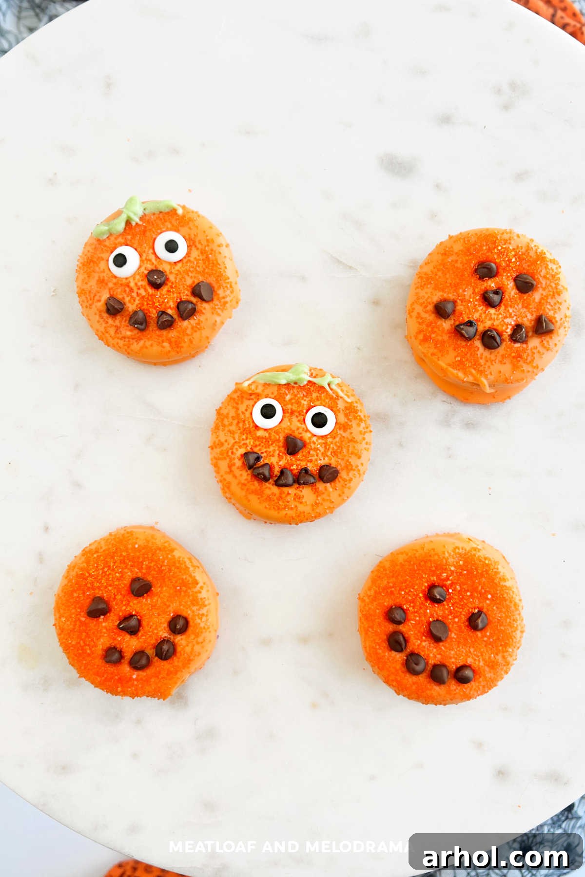 Halloween Oreo pumpkins with bright orange candy melts, expressive candy eyes, and mini chocolate chip mouths, resting on wax paper.