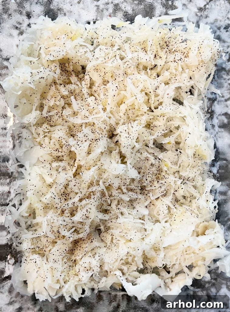 Sauerkraut seasoned with salt and pepper spread in a baking dish.