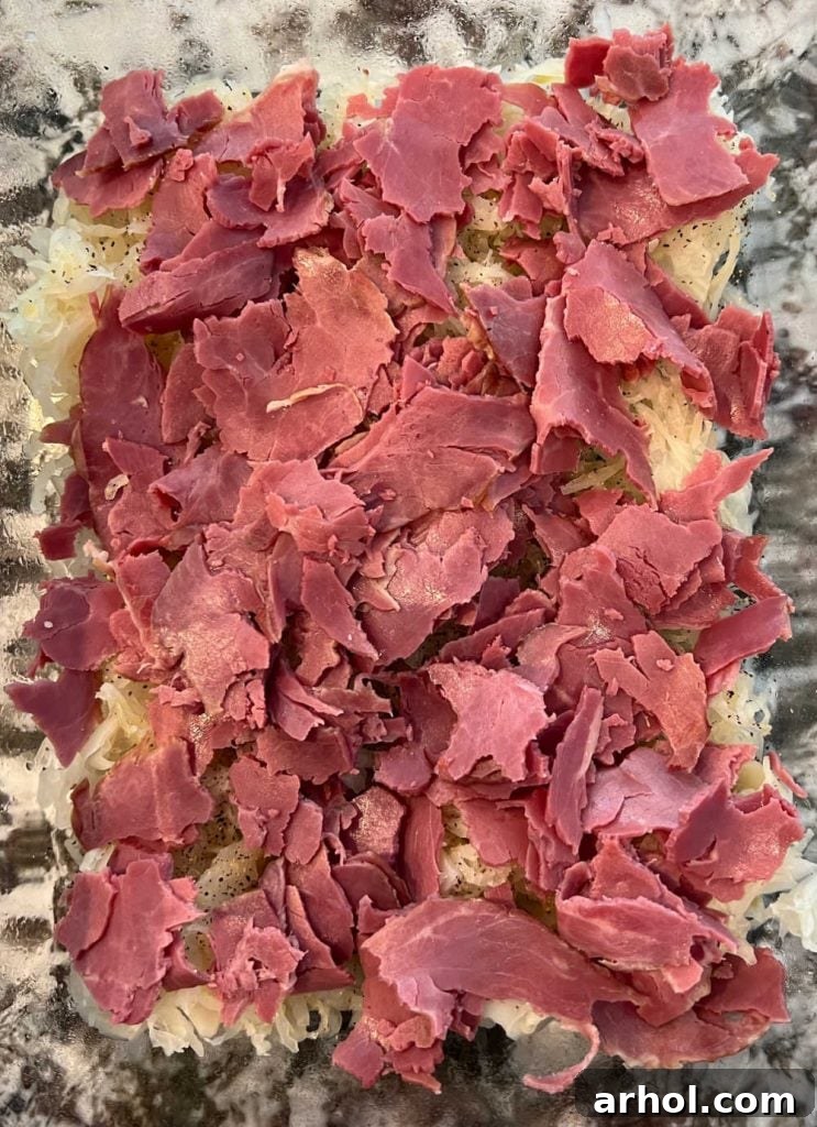 Sliced corned beef layered over sauerkraut in a baking dish.