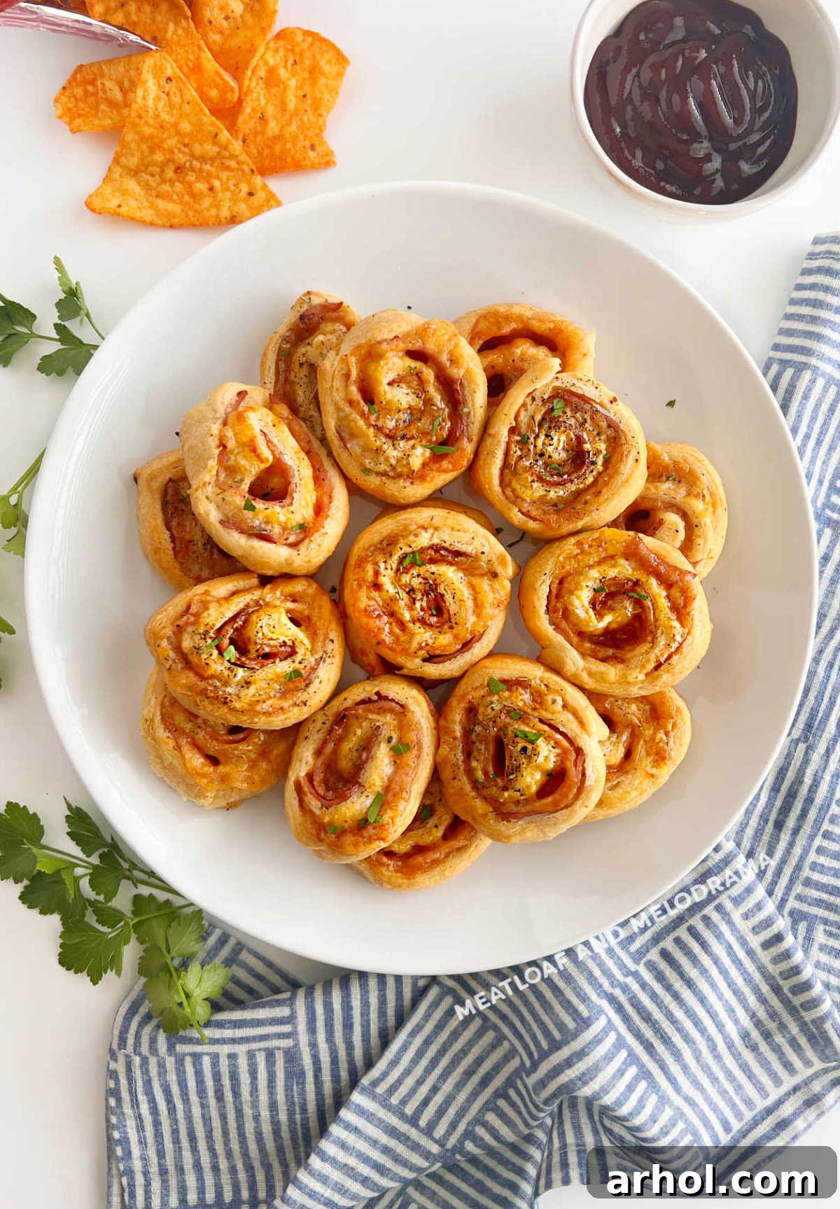Crispy Ham & Cheese Crescents 2 Golden brown baked ham and cheese crescent roll ups garnished with fresh parsley on a serving platter.
