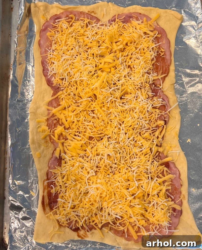 Crispy Ham & Cheese Crescents 5 Crescent dough sheet topped with a layer of ham slices and evenly sprinkled shredded cheese, ready for rolling.
