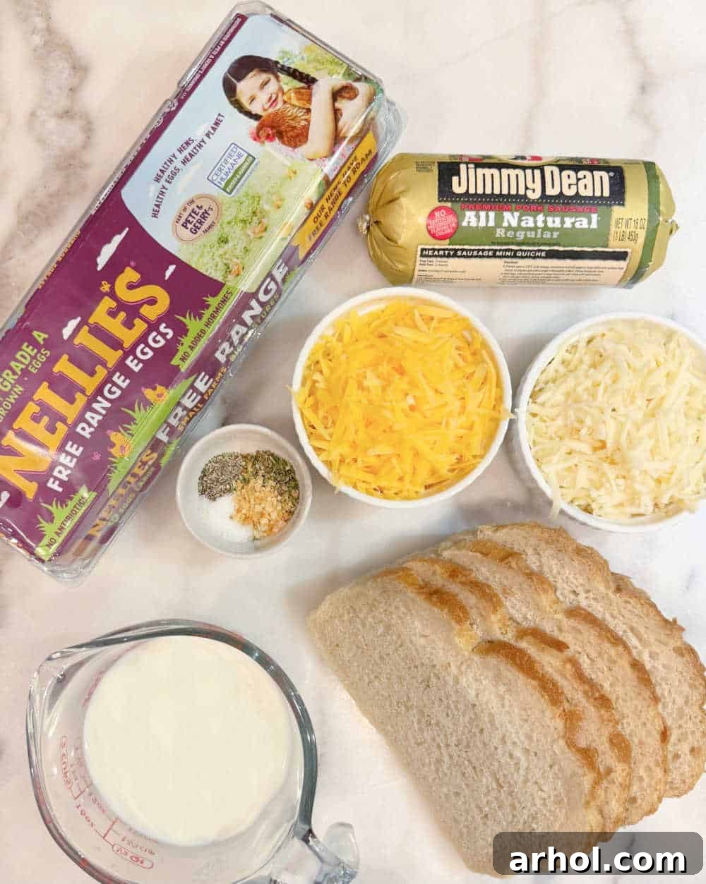 A flat lay showing all the fresh ingredients needed for the sausage egg and cheese casserole: eggs, sliced sourdough bread, breakfast sausage, mixed shredded cheese, milk, and various spices.