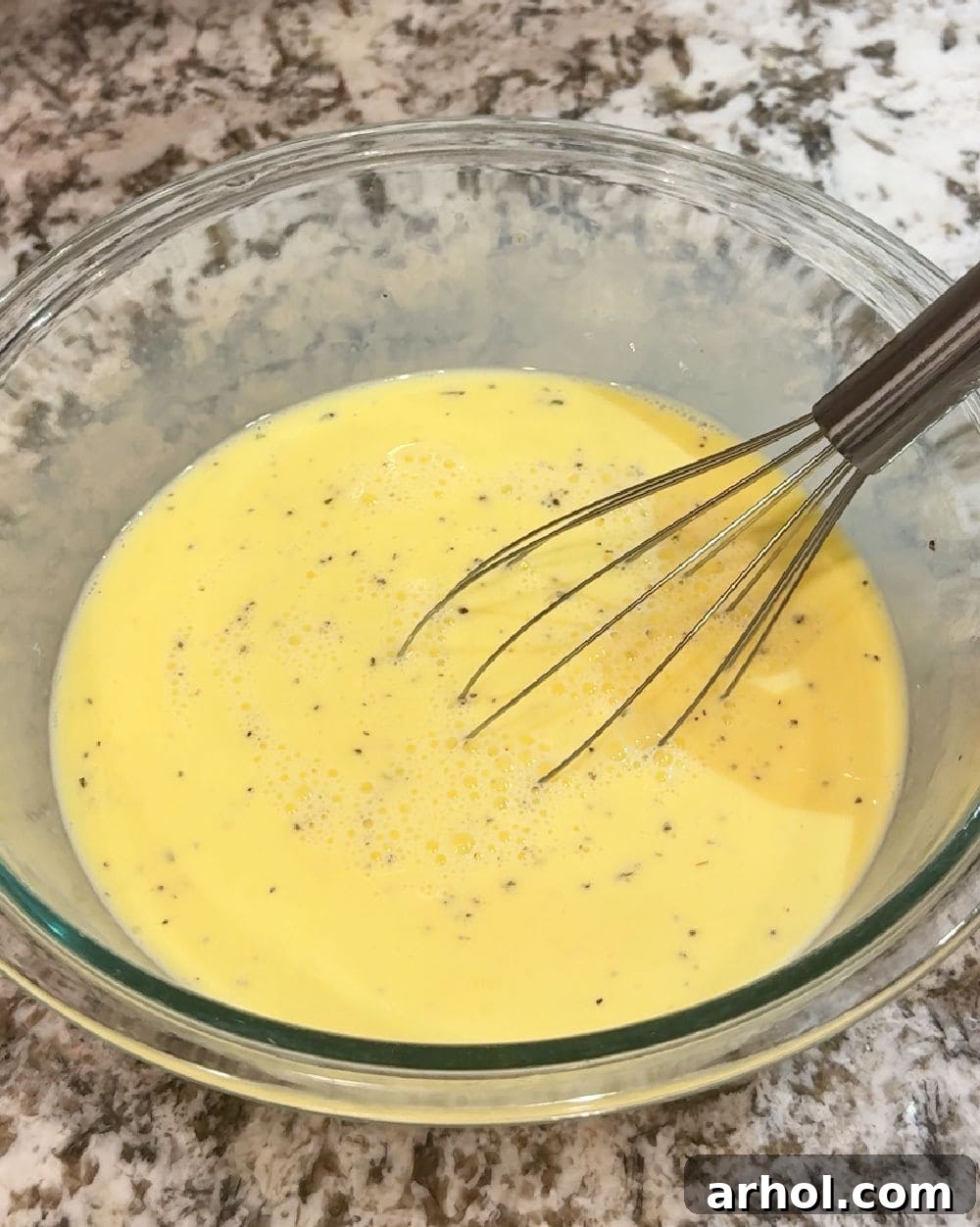 Whisking eggs, milk, salt, and pepper vigorously in a large mixing bowl.