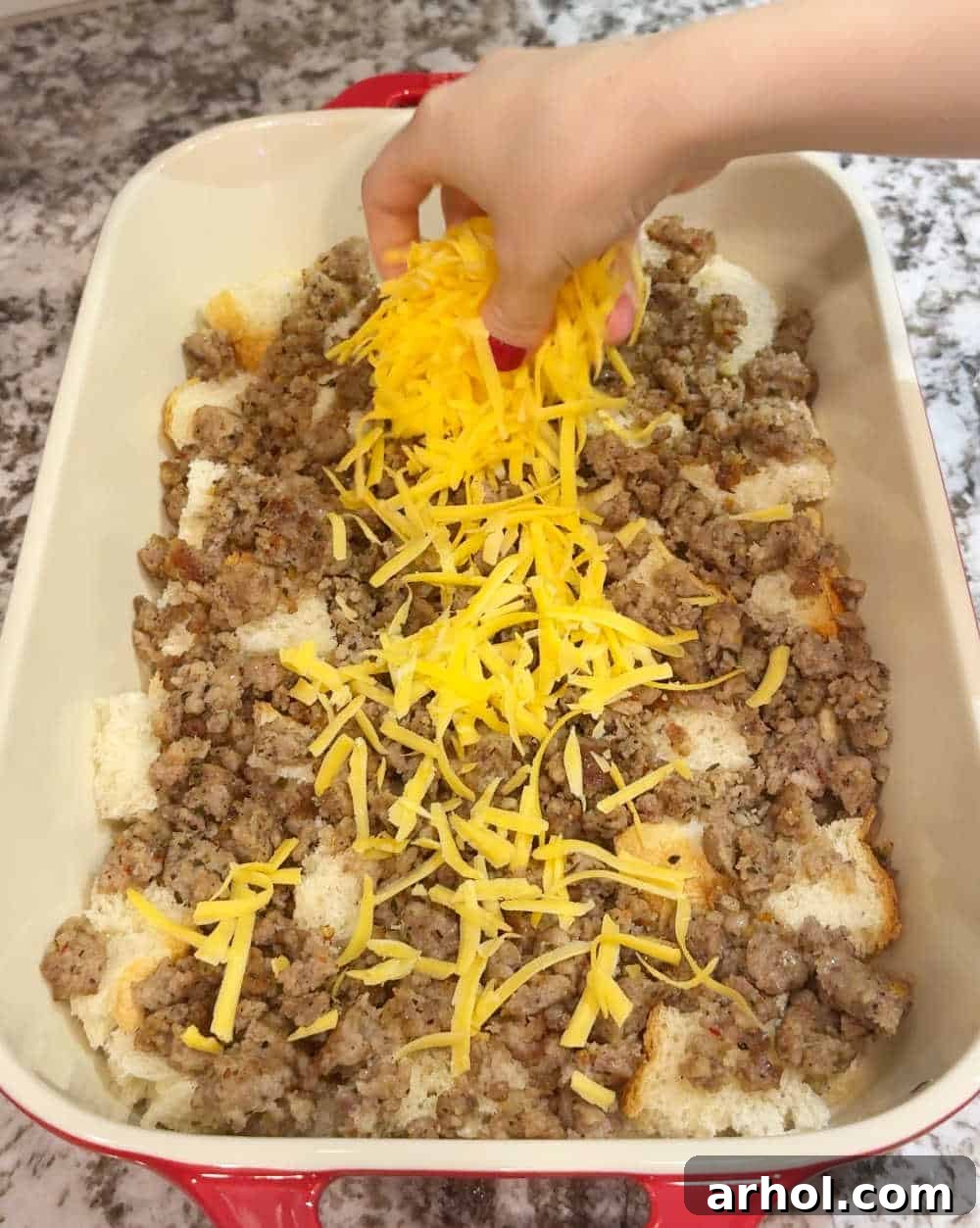 Topping the layered sourdough bread and sausage with shredded cheddar and pepper jack cheese.