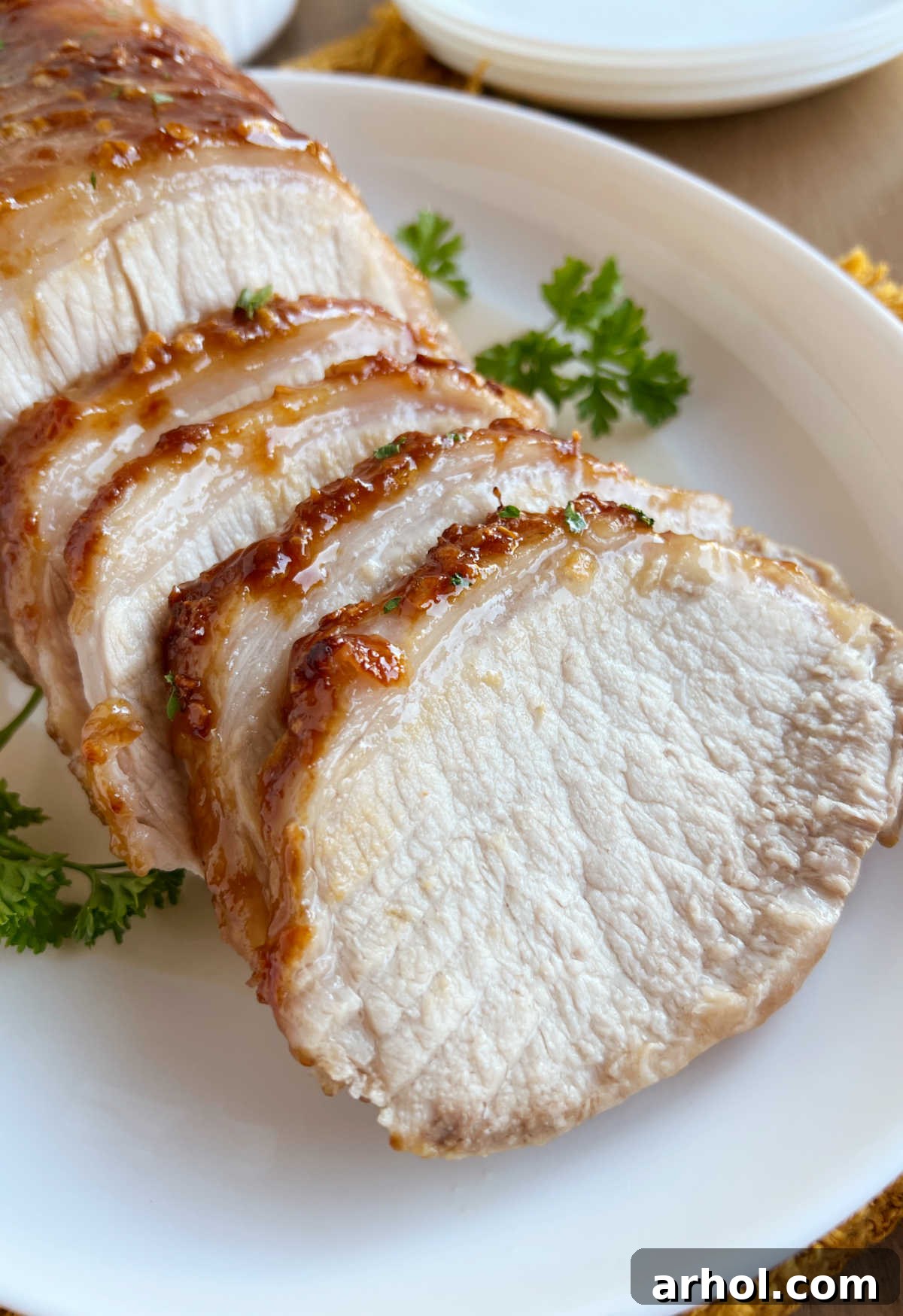 Sliced roast pork with maple and mustard glaze on a platter, garnished with fresh parsley.