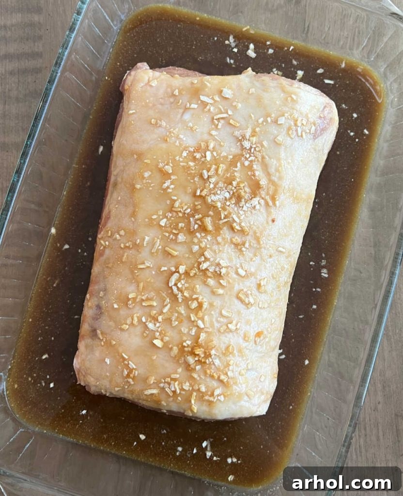 Pouring maple glaze over a pork roast in a baking dish, ready for the oven.