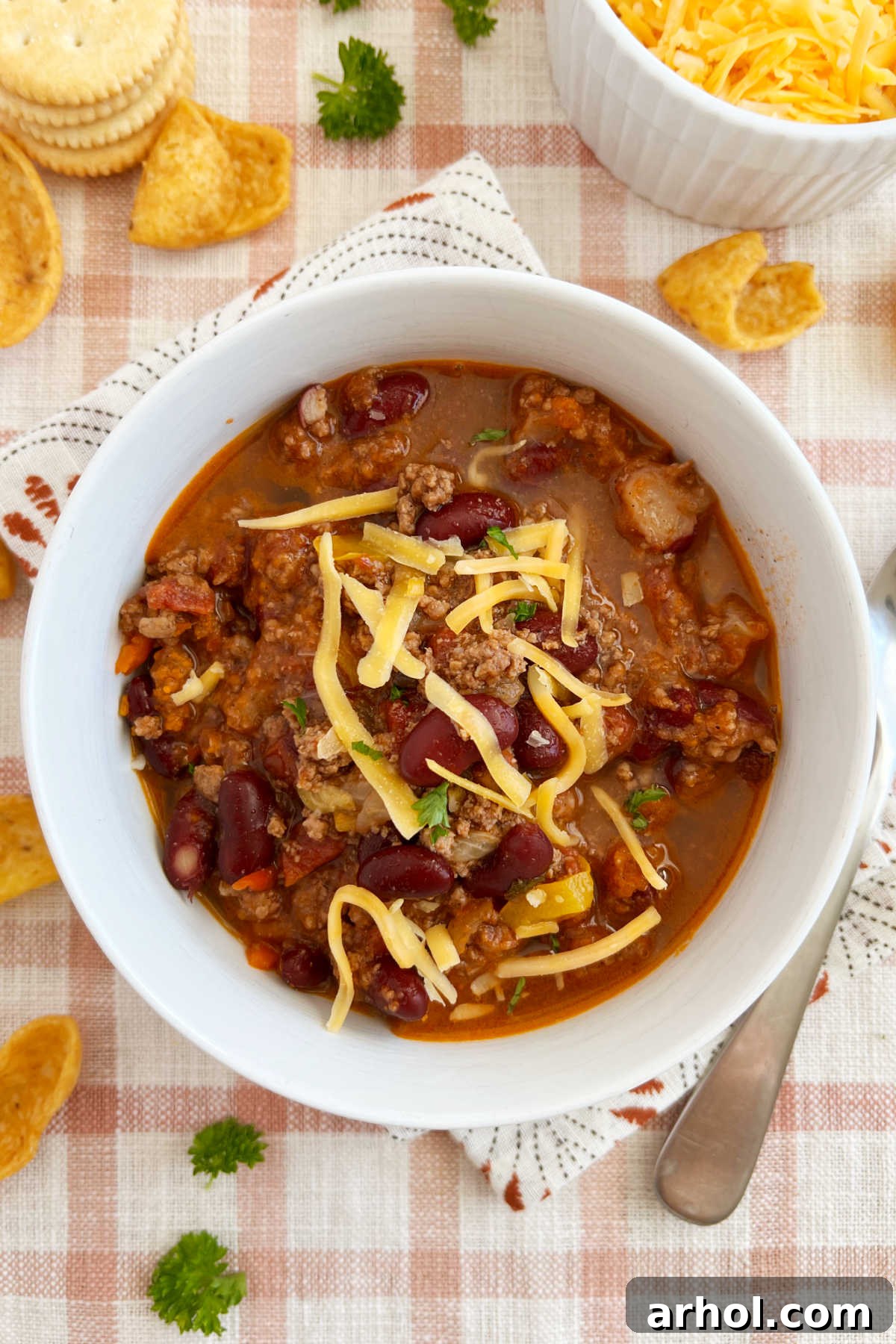 A steaming bowl of Mom's Best Mild Chili with ground beef, kidney beans, and a generous sprinkle of shredded cheese, freshly cooked on the stovetop.