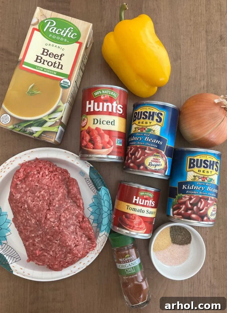 Fresh ingredients laid out for making chili, including ground beef, ripe tomatoes, kidney beans, a vibrant bell pepper, a yellow onion, and a selection of dried spices.