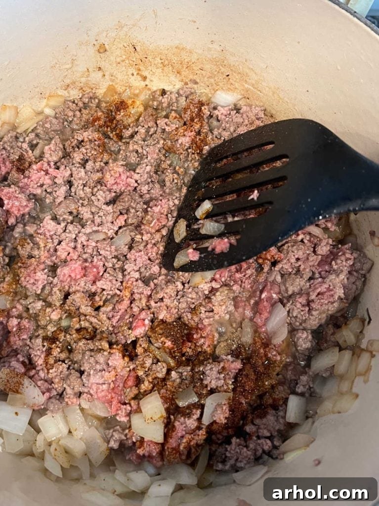 Close-up of browned ground beef and softened onions simmering in a sturdy Dutch oven on the stovetop, forming the flavorful base for the chili.