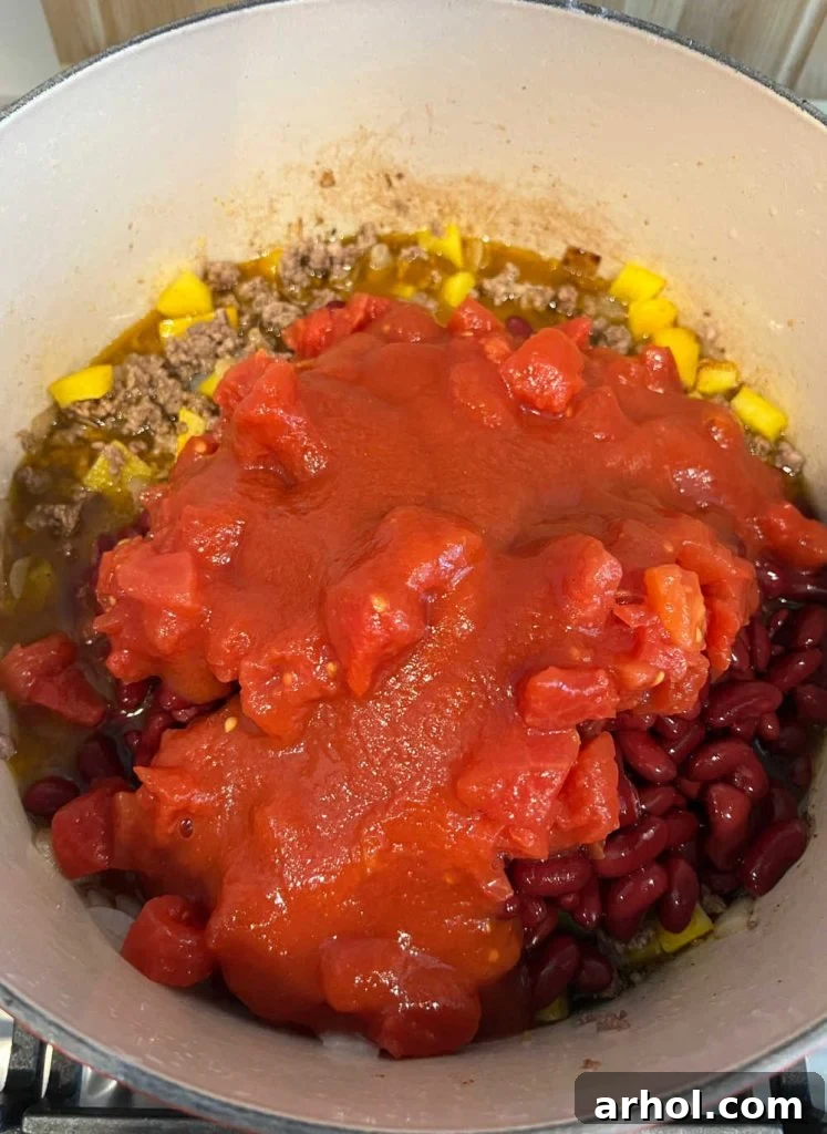 All the core chili ingredients—ground beef, colorful bell peppers, kidney beans, and tomatoes—stirred together and simmering gently in a large Dutch oven on the stovetop.