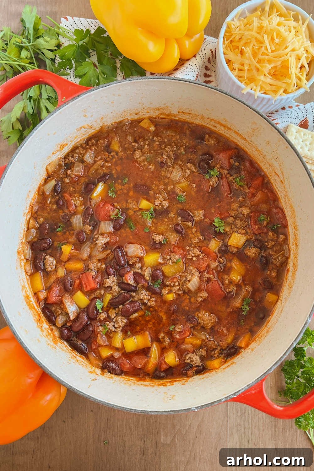 A large pot of Mom's Best Mild Chili with ground beef and kidney beans, served in a rustic Dutch oven on a wooden table, adorned with an assortment of fresh toppings.