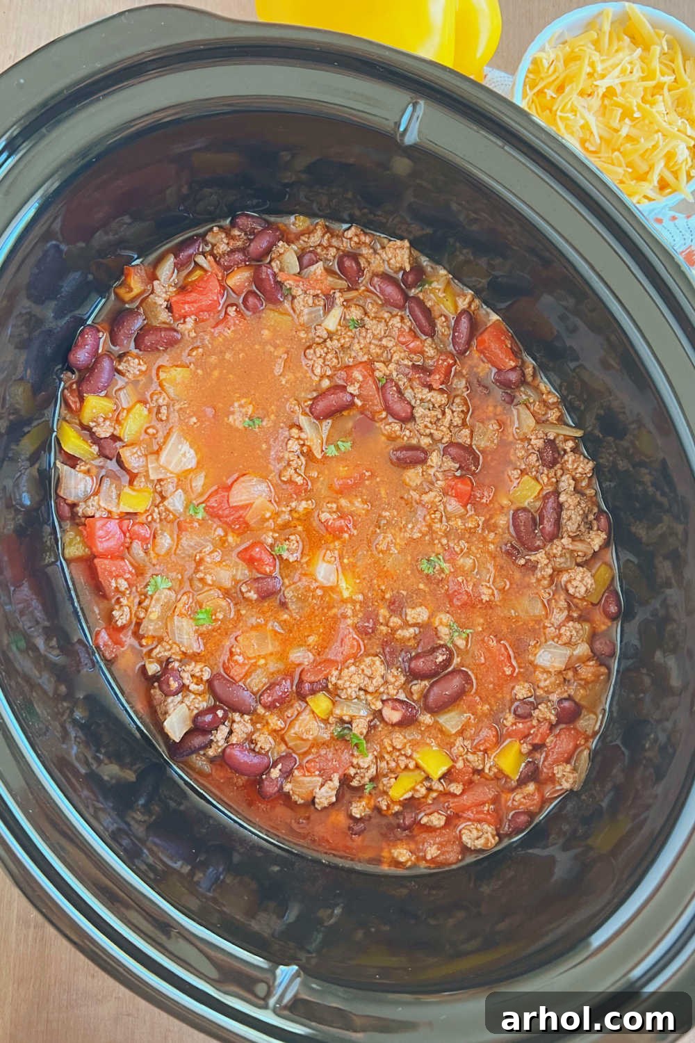 Mom's Best Mild Chili with ground beef and kidney beans simmering gently in a crockpot slow cooker, emitting a comforting aroma.
