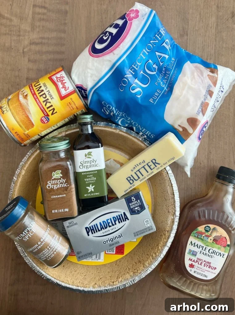 Ingredients laid out for no bake pumpkin cheesecake pie including graham cracker pie crust, canned pumpkin puree, cream cheese, butter, powdered sugar, vanilla extract, pumpkin pie spice, ground cinnamon, and maple syrup.