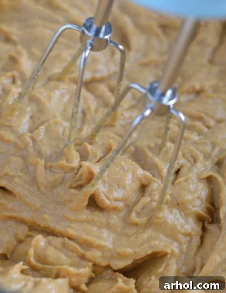 Mixing pumpkin puree, pumpkin pie spice, cinnamon, and maple syrup into the cream cheese filling in a large mixing bowl.