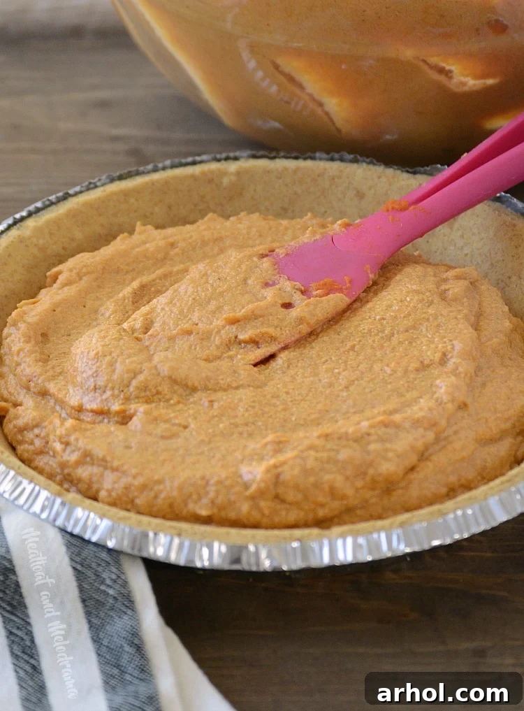 Spreading the smooth pumpkin cheesecake filling evenly into a graham cracker pie crust.