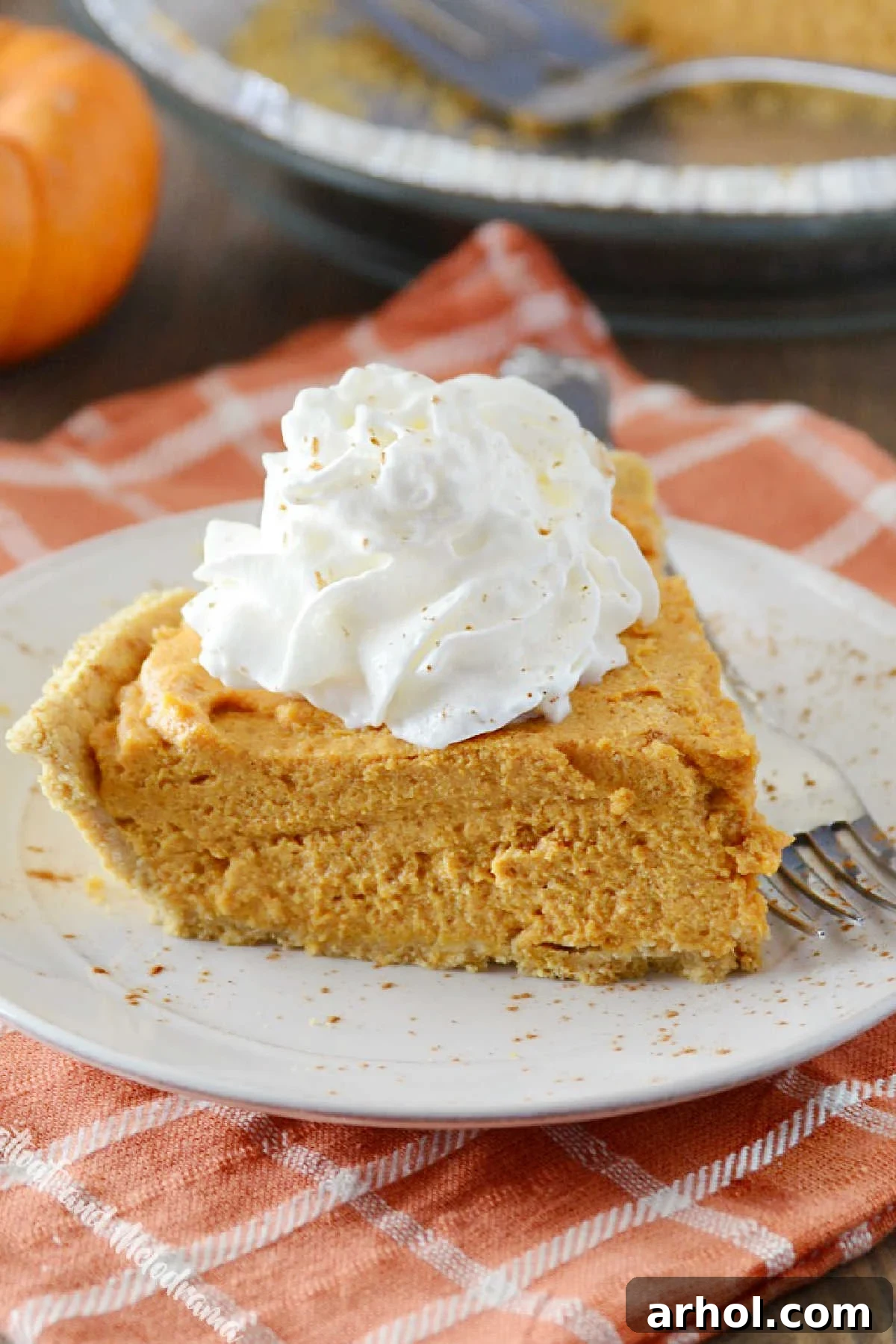 A beautiful slice of no bake pumpkin pie with a dollop of fresh whipped cream on a white plate, ready for dessert.