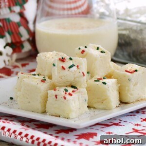 Creamy Fantasy Eggnog Fudge squares arranged beautifully on a plate, with a glass of eggnog in the background, ready for holiday enjoyment.