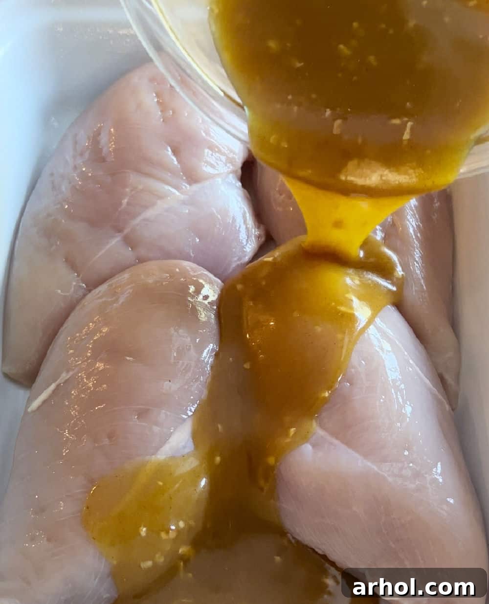 Pouring the luscious honey mustard curry sauce over chicken in a baking dish.