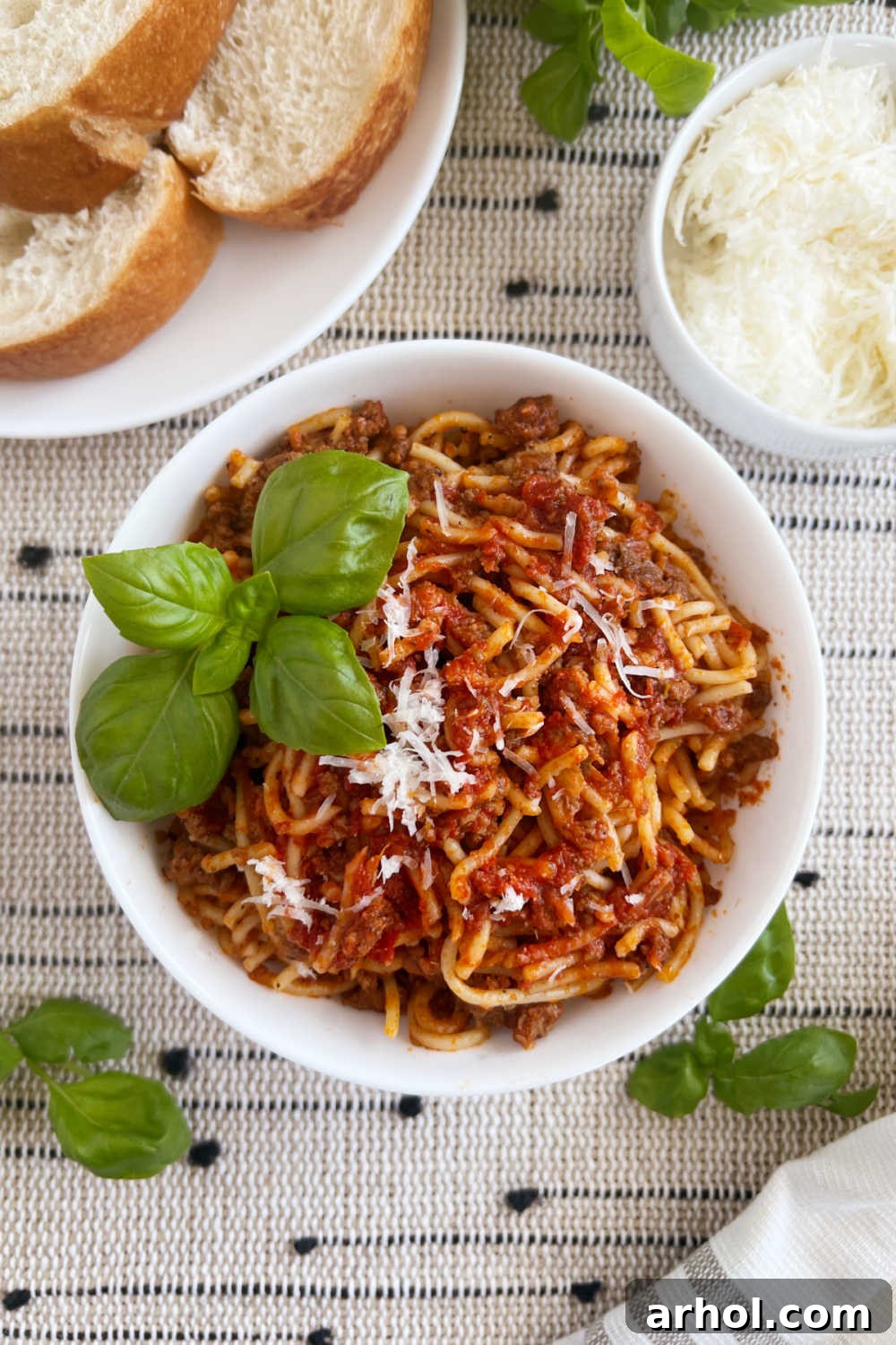 Instant Pot spaghetti and meat sauce in white bowl with fresh basil, Parmesan cheese, and crusty bread