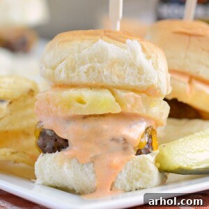 Spicy habanero beef sliders with pineapple and cheddar cheese on white plate with pickle and chips