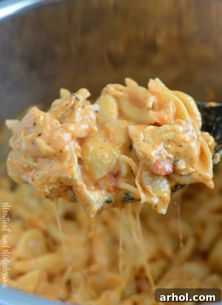Cheesy Instant Pot creamy chicken pasta being scooped onto a spoon, showing the rich sauce and perfectly cooked shells
