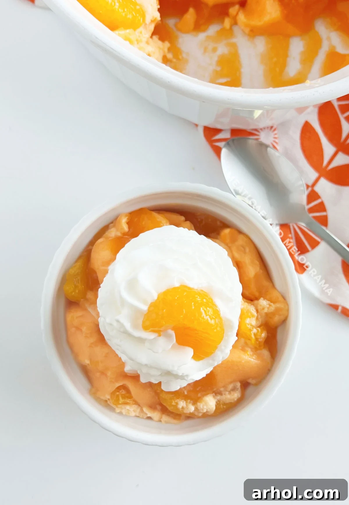 A beautiful bowl of orange jello salad garnished with fresh mandarin orange slices, ready to be served on a table.
