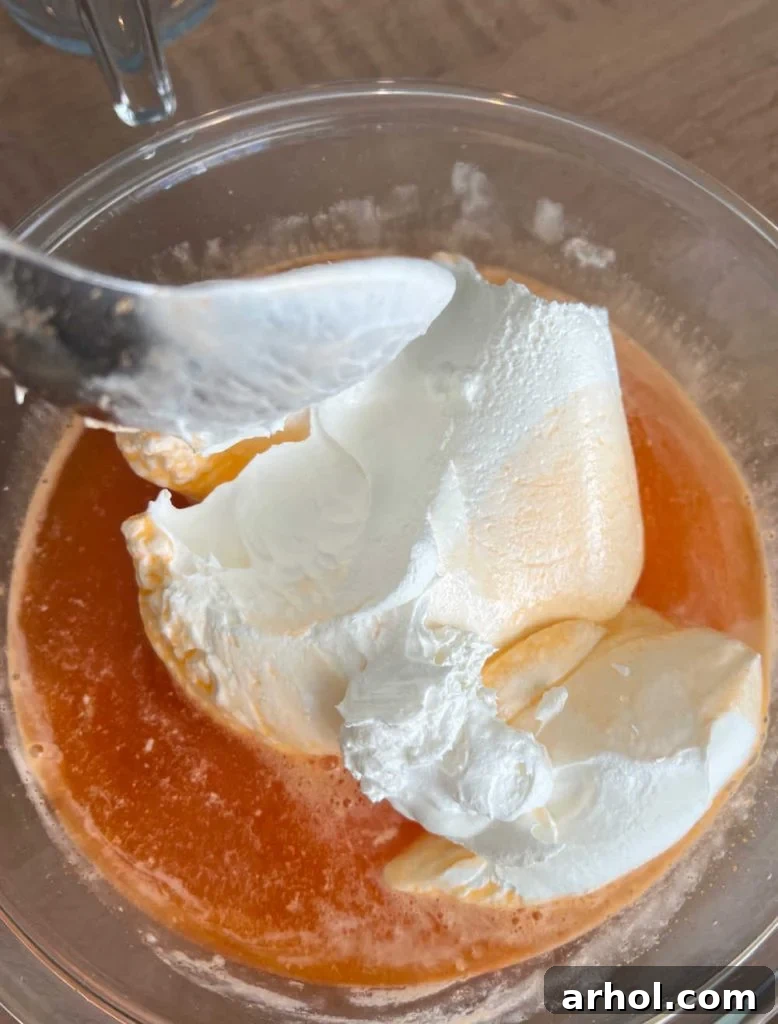 Mixing cool whip with partially set orange jello in a mixing bowl using an electric mixer.