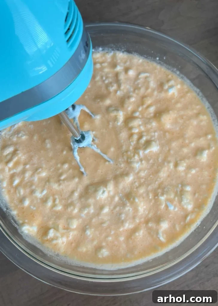 The process of mixing Cool Whip into the thickened orange Jello using an electric mixer.
