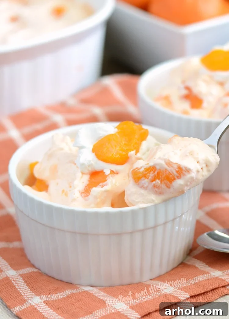 Individual serving of orange jello fruit salad with mandarin orange slices in a white ramekin.
