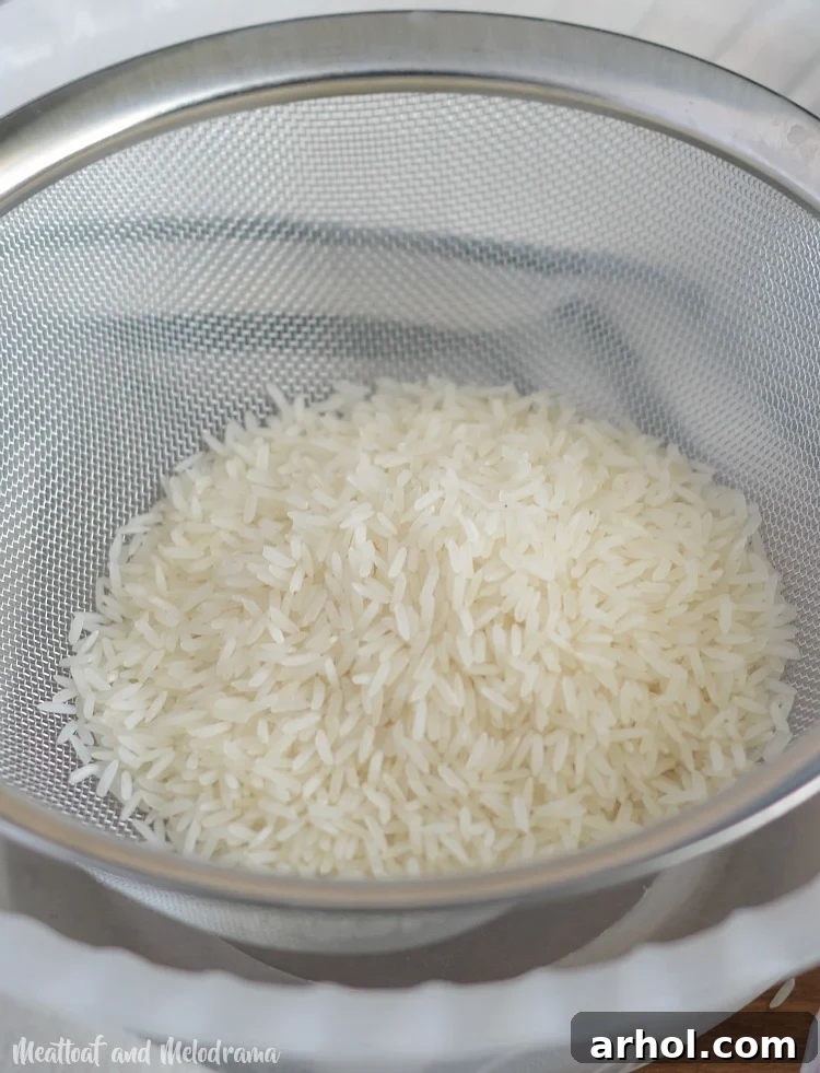 Jasmine rice being rinsed thoroughly in a fine mesh strainer under cold water.