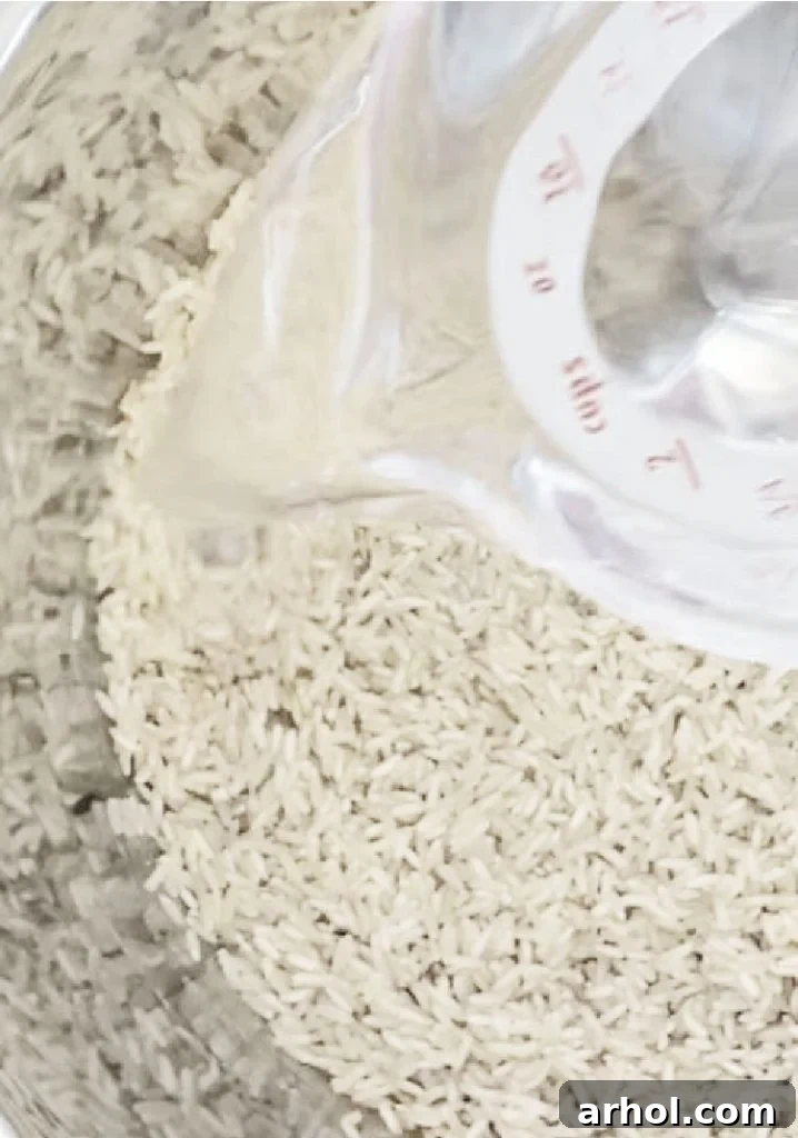 Cold water being poured over jasmine rice, sea salt, and olive oil in the Instant Pot inner pot.