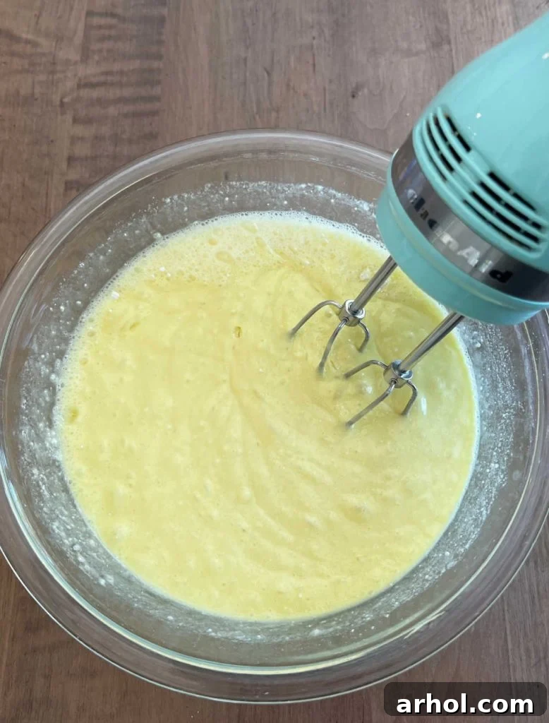 An electric mixer blending the cake mix and Sprite soda in a large bowl, creating a smooth and light green batter.