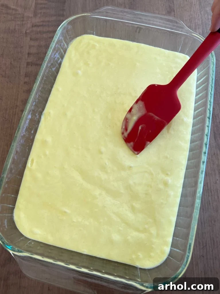 Smooth, light green cake batter being spread evenly into a greased rectangular baking pan with a silicone spatula.