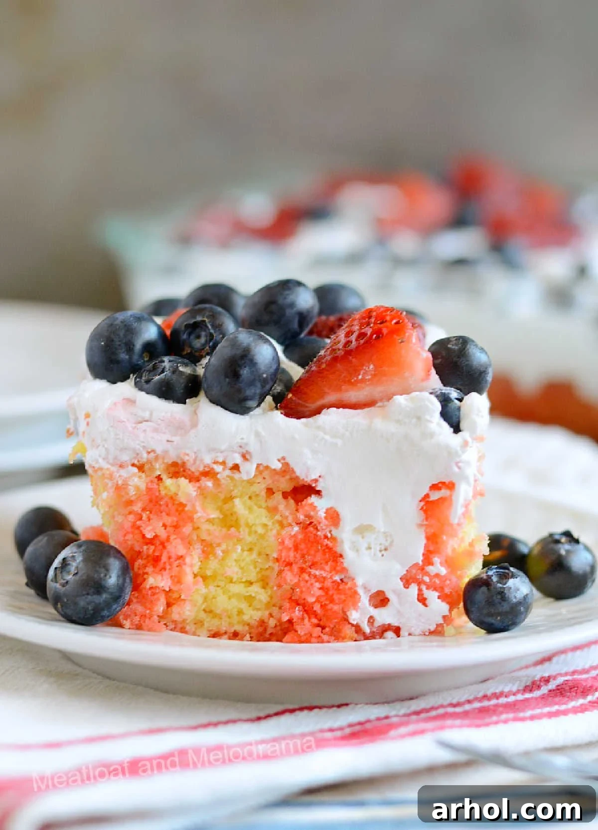 Slice of red, white, and blue poke cake with cool whip, strawberries, and blueberries on a plate, ready to be enjoyed at a patriotic celebration.