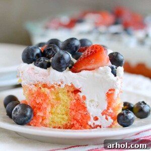Slice of red, white, and blue poke cake with strawberries and blueberries on a plate, ready to be served at a patriotic gathering.