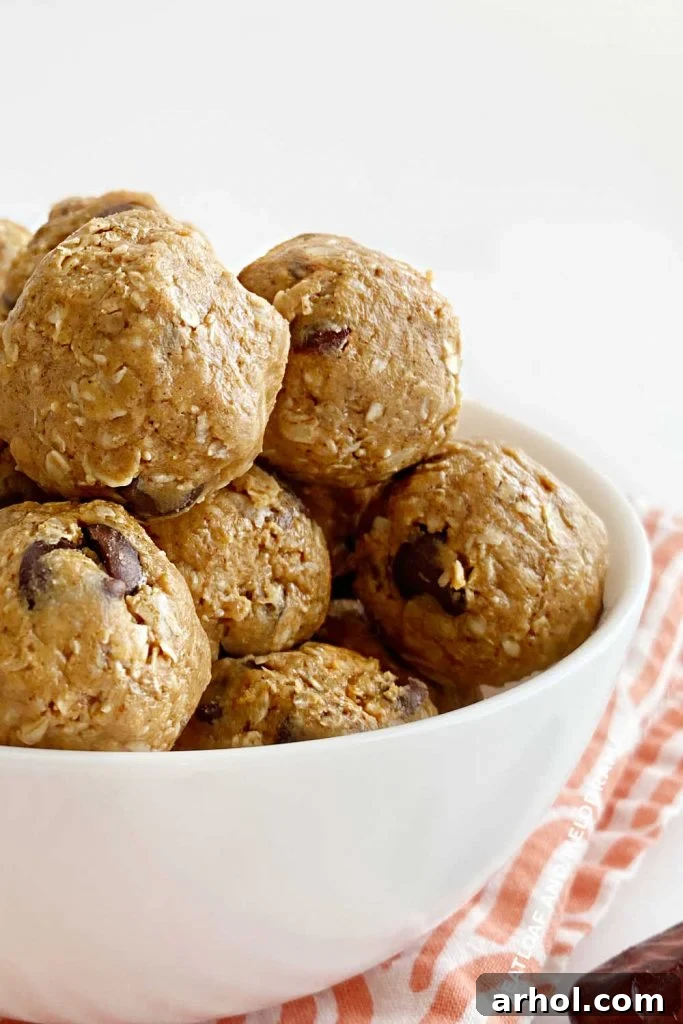 Close-up view of a pile of no-bake energy balls with visible oats, peanut butter, and chocolate chips in a white bowl.