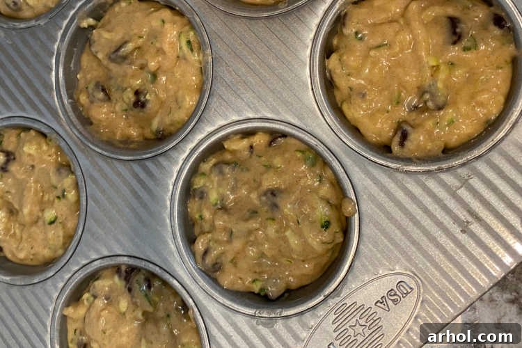Raw banana zucchini muffin batter evenly distributed in a greased muffin tin, ready for baking.