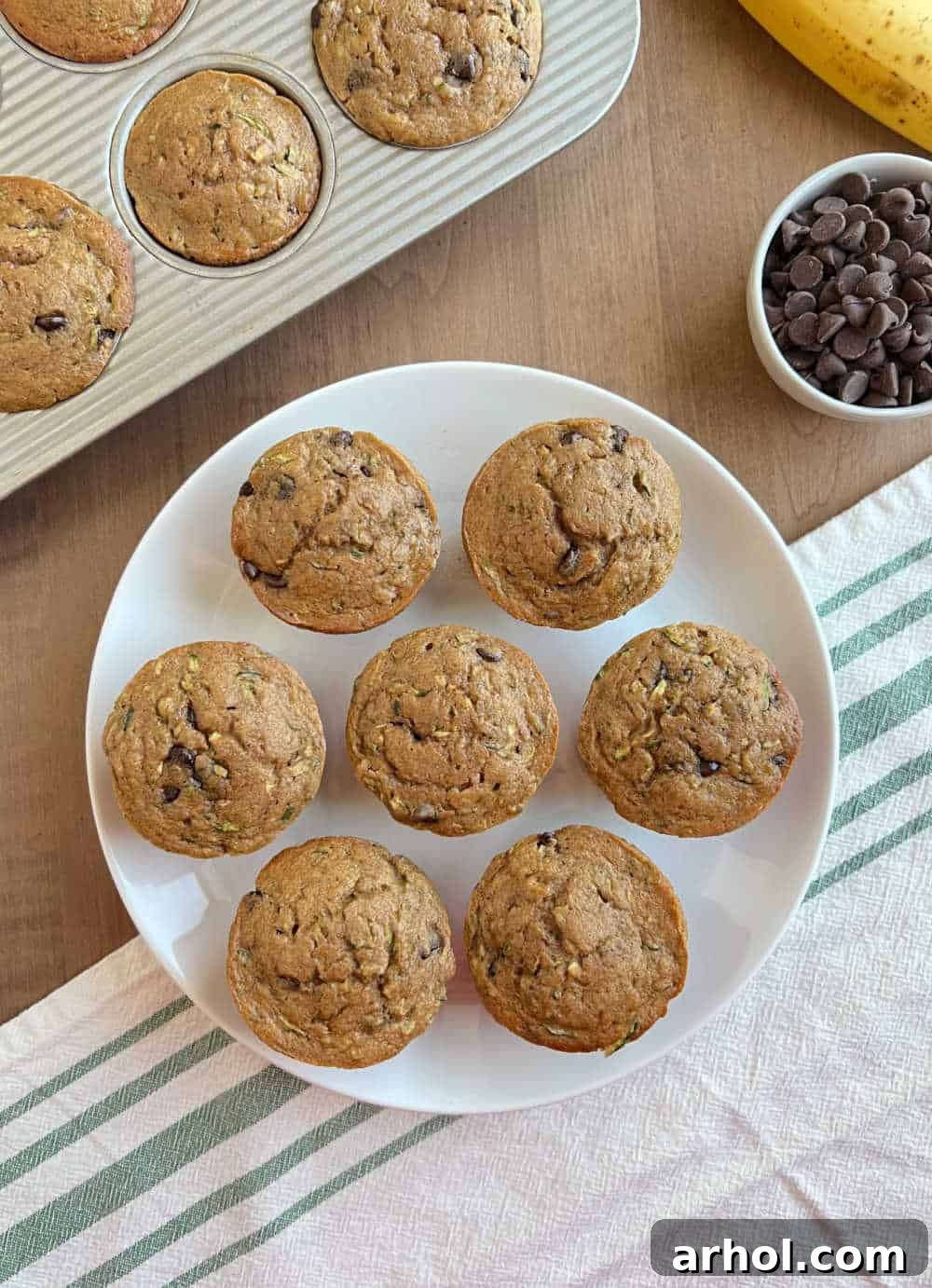A plate stacked high with freshly baked, moist zucchini banana chocolate chip muffins, ready to be served.